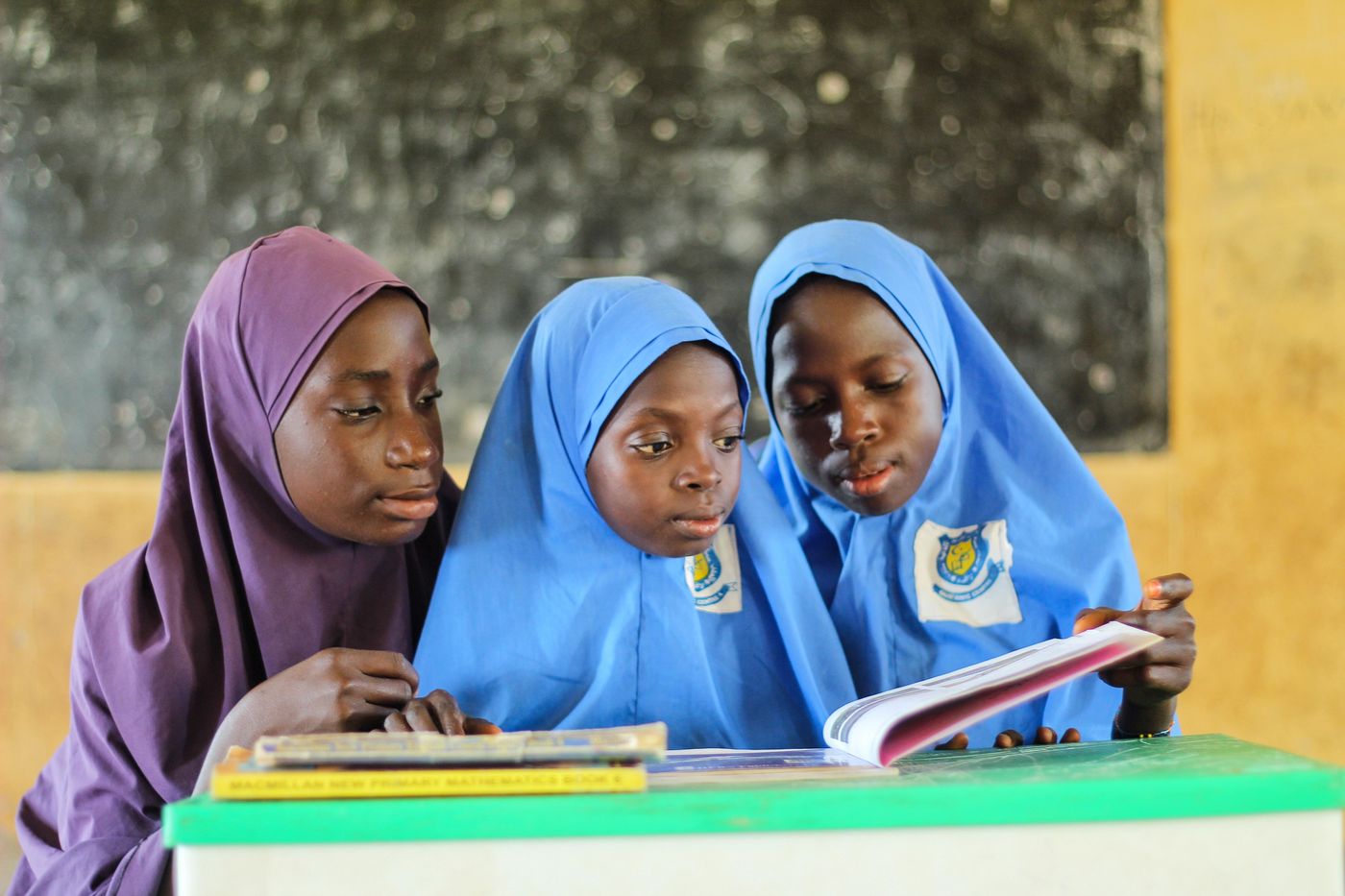Three students in headscarves reading a book together in a classroom