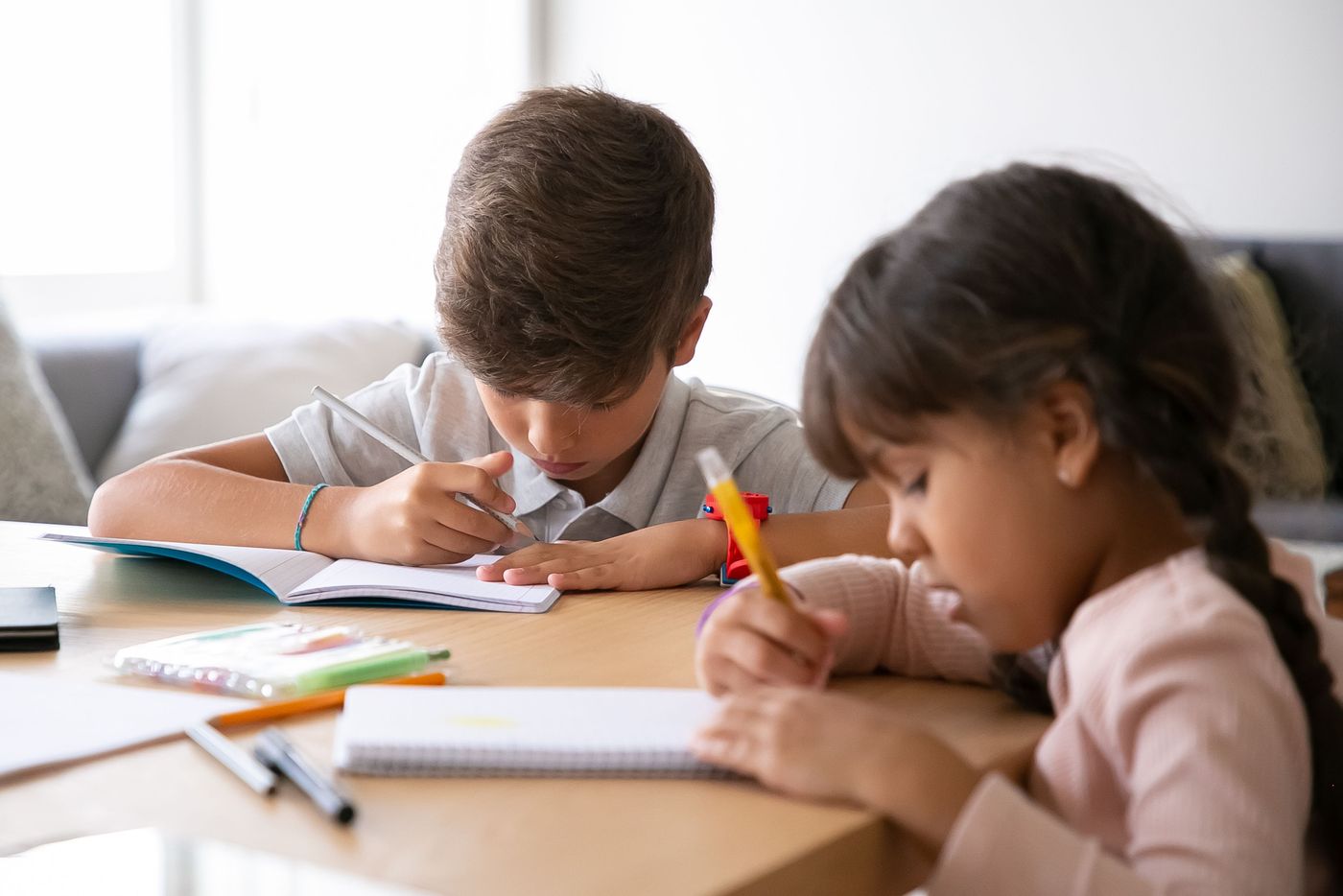 A boy and a girl writing at a table with books and notebooks